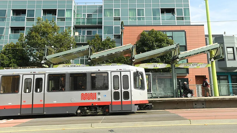 A Muni street car train on Third Street in front of residential buildings in Mission Bay.