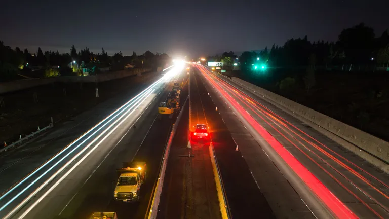 A long-exposure photo shows cars streaking down the highway at night.