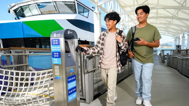 Two smiling youths use their smart phones to pay for public transit.