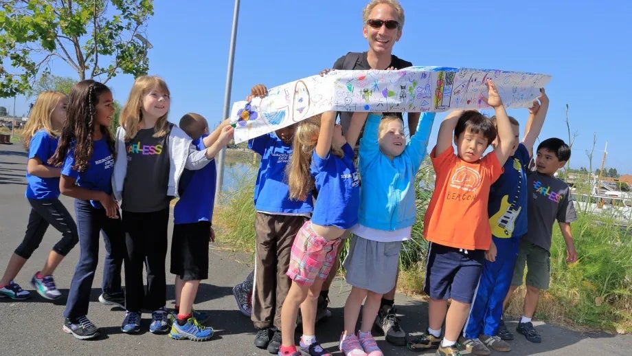 Beacon Day School students proudly display their artwork in support of the Bay Trail; Kurt Schwabe pauses for a photo op with the kids before resuming his 30-day trek around the San Francisco Bay.