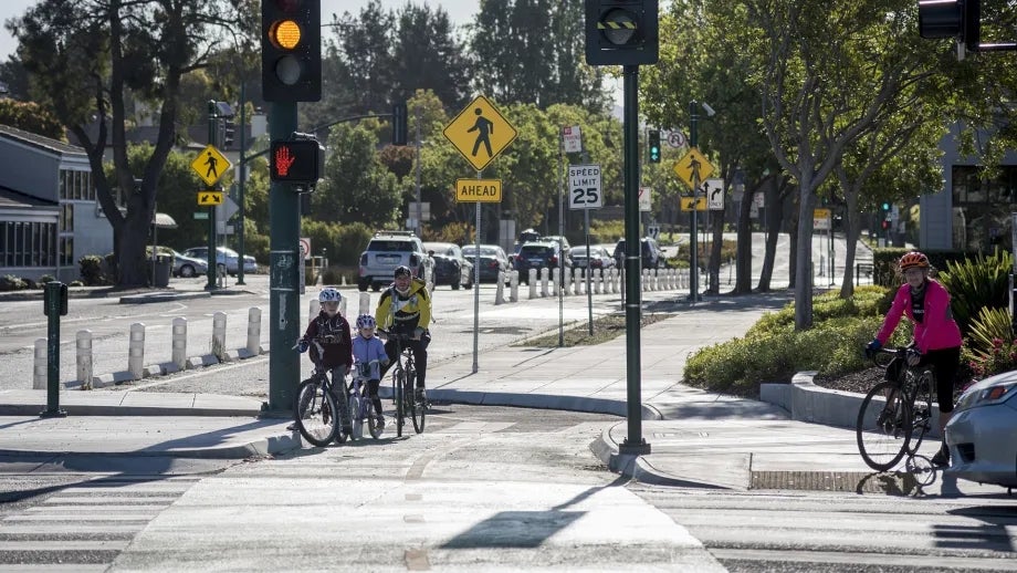 Several adults and children on bicycles wait in separated bike lanes at a Berkeley intersection that is also used by vehicles.