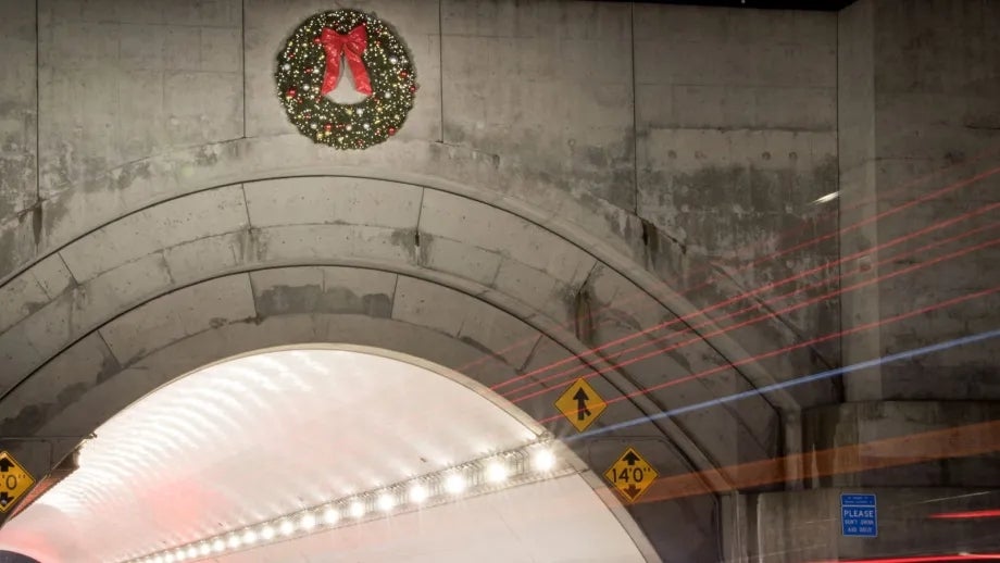 Tail lights streak red as vehicles enter the entrance of westbound Yerba Buena tunnel with the holiday wreath hung above.